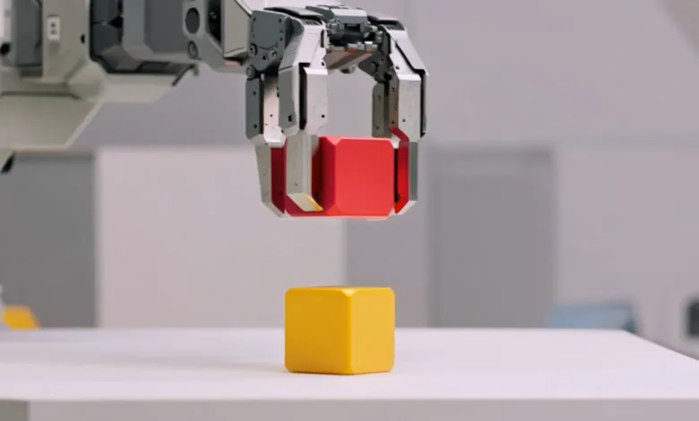 Robotic arm holding red cube above yellow cube on white surface.