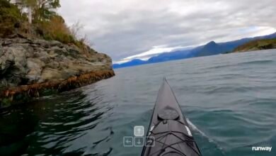First-person view from a kayak on a body of water near a rocky shoreline.