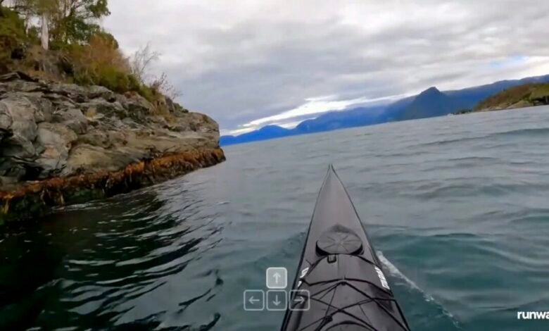 First-person view from a kayak on a body of water near a rocky shoreline.