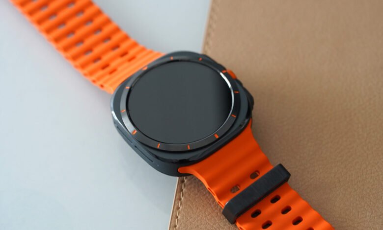 Close-up of a smartwatch with a bright orange band on a textured surface.