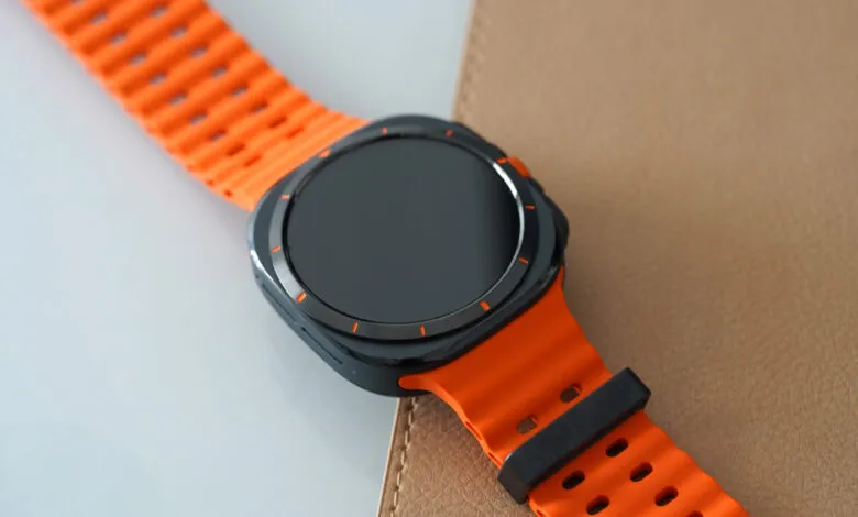 Close-up of a smartwatch with a bright orange band on a textured surface.