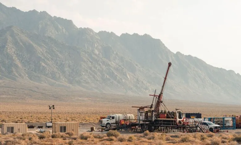Geothermal drilling rig in desert landscape with mountains in background.
