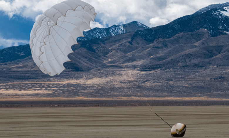 White parachute and payload on a flat, dry lakebed with mountains in background.