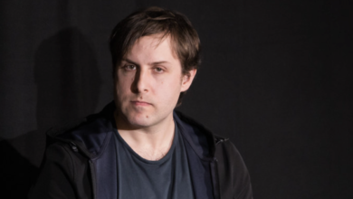 Portrait of a man with brown hair and a serious expression against a dark background.