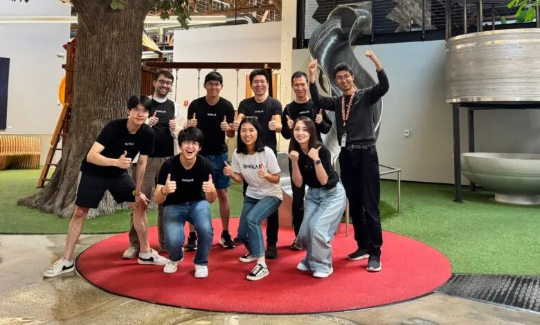 Enthusiastic team of nine giving thumbs up in a playful office setting.