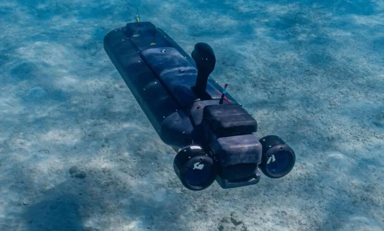 Underwater drone exploring sandy ocean floor in clear blue water.