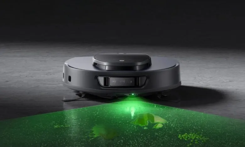 Robot vacuum cleaner emitting green light to detect dirt on a gray floor.