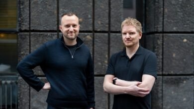 Two men stand side-by-side against a textured gray stone wall.