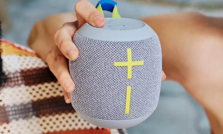 Person holding a gray Ultimate Ears Wonderboom speaker with yellow accents.
