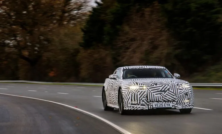 Camouflaged car driving on a road through a wooded area.