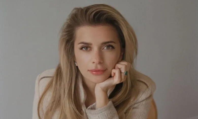 Portrait of a woman with blonde hair resting her chin on her hand.