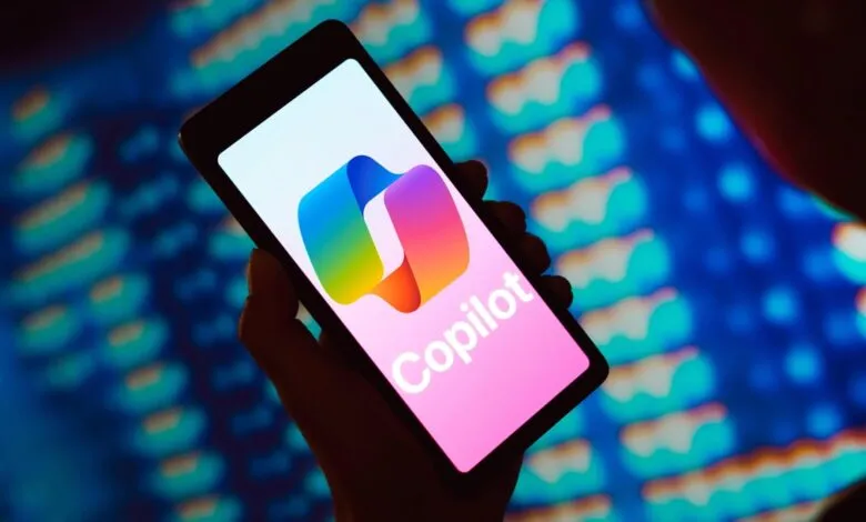 Hand holding phone displaying Copilot app logo against a blue background.