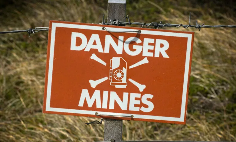 Orange 'Danger Mines' sign with skull and crossbones on a wooden post.
