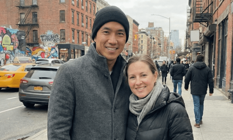 Smiling couple poses on a city street with buildings and traffic.