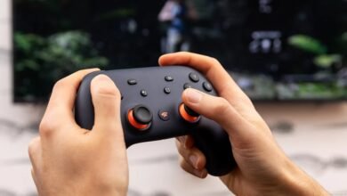 Hands holding a Google Stadia controller in front of a TV.