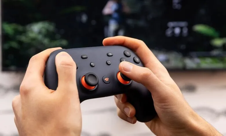 Hands holding a Google Stadia controller in front of a TV.