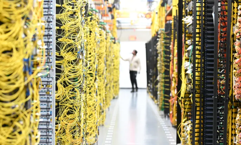 Data center aisle with server racks and colorful cables, technician in background.