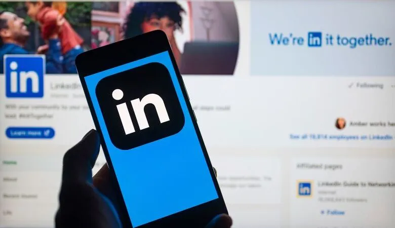 Person holding phone displaying LinkedIn app logo against LinkedIn website.
