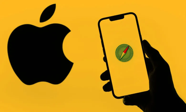 Apple Safari browser on iPhone held by hand against Apple logo backdrop.