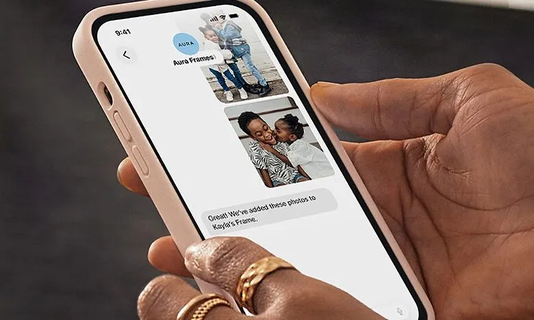 Hand holding phone displaying Aura Frames app with shared family photos.