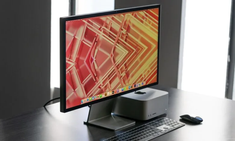 Studio Display and Mac Studio setup on a dark desk with a modern, geometric wallpaper.