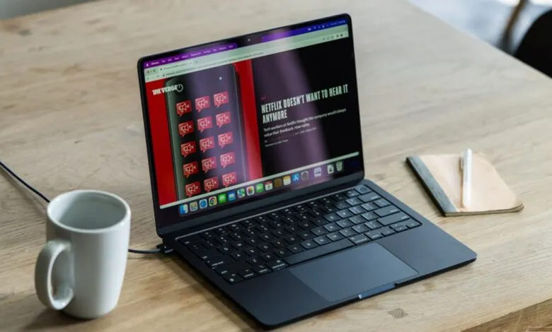 Laptop displaying 'Netflix Doesn't Want to Hear It Anymore' article on wooden desk with coffee and notebook.