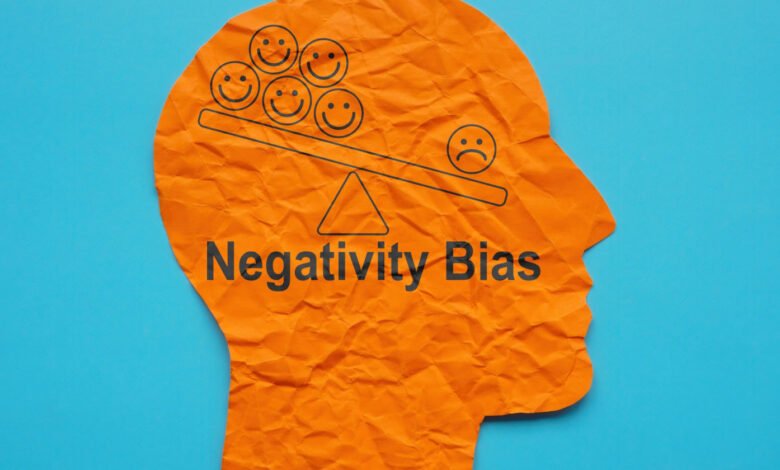 Orange head silhouette shows negativity bias with happy/sad faces on a scale.