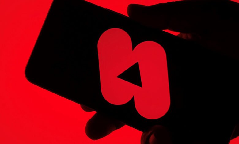 Hand holds smartphone displaying the YouTube Shorts logo on a red screen.