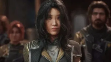 Close-up of a woman with dark hair and a serious expression, surrounded by others.