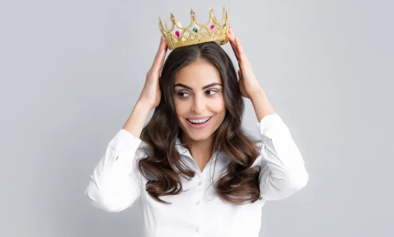 Woman with crown on head, smiling and looking to the side.