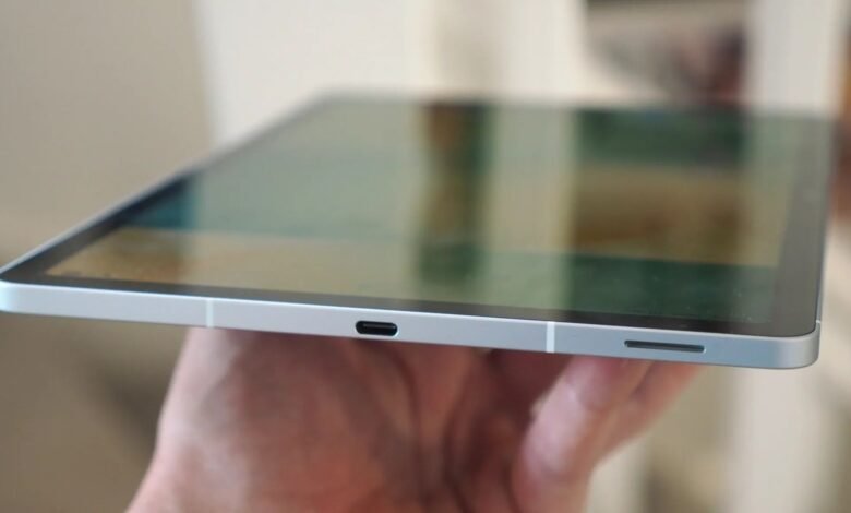 Silver tablet held in hand, showing USB-C port and slim design.