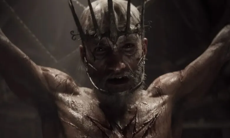 Man with crown and scars, arms raised, looking distressed.