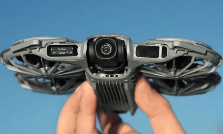 Close-up of a gray drone held in a hand against a clear blue sky.