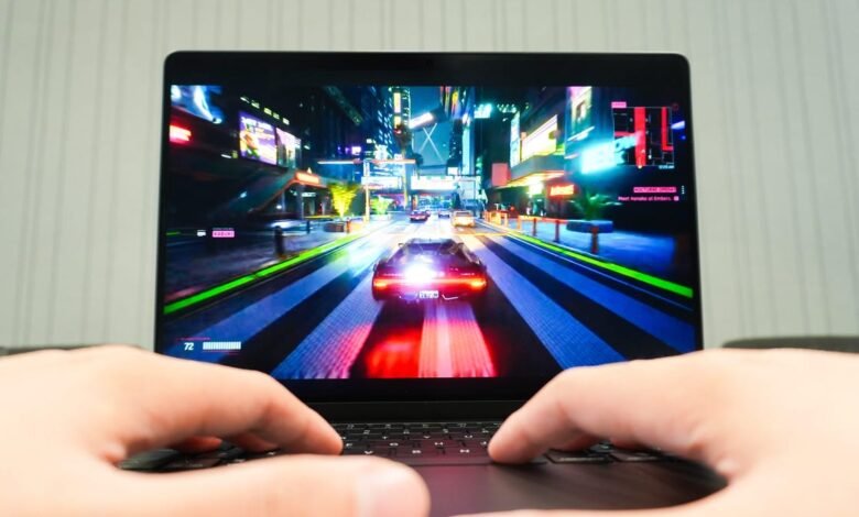 Laptop screen displays Cyberpunk 2077 gameplay with hands on keyboard.