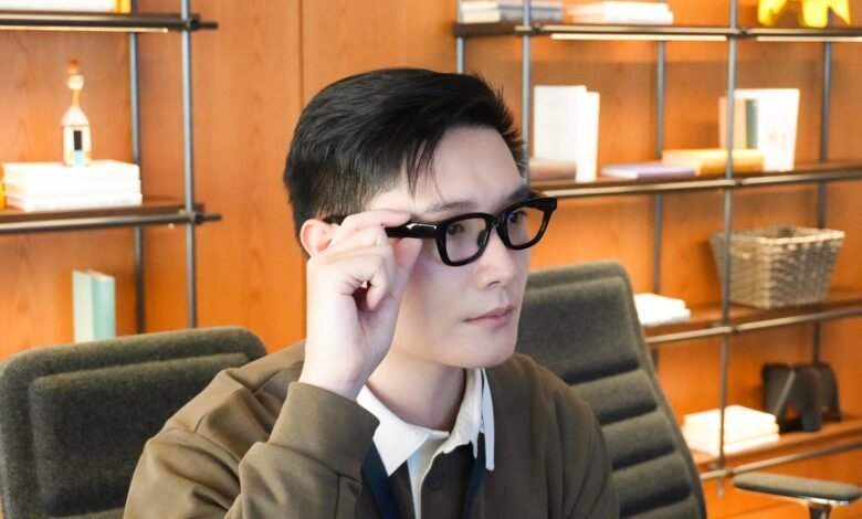 Person wearing black-framed glasses in an office setting.