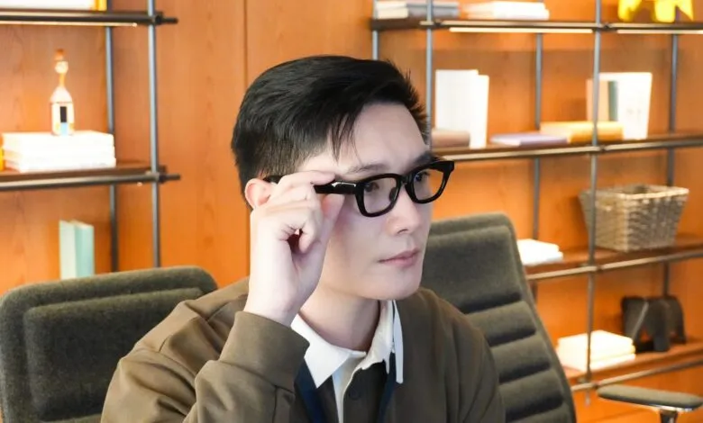 Person wearing black-framed glasses in an office setting.