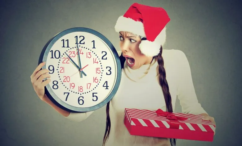 Woman in Santa hat looks shocked at clock while holding gift.