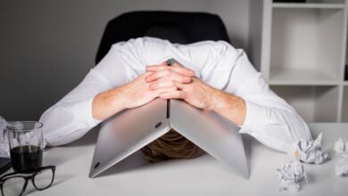 Person with head under laptop, expressing frustration or burnout.
