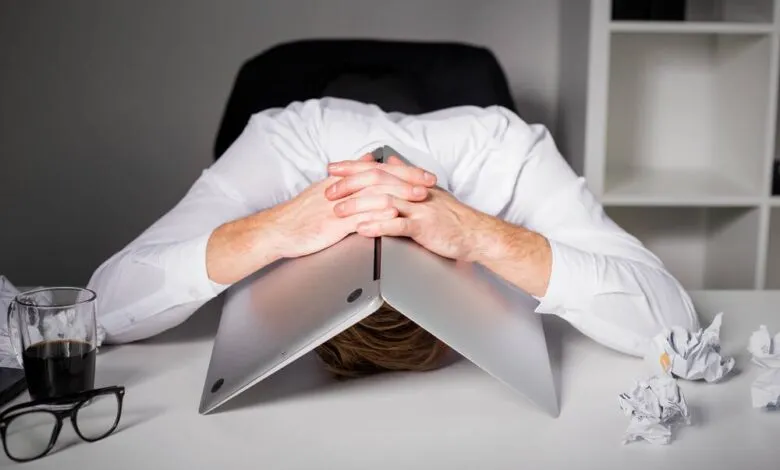 Person with head under laptop, expressing frustration or burnout.