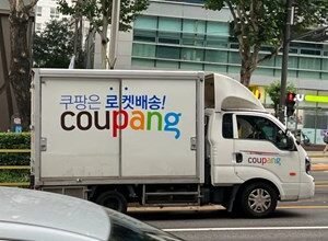 Coupang delivery truck on a city street with Korean text and Coupang logo.