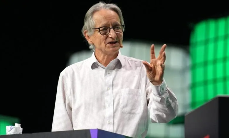 Man with glasses gestures while speaking on stage at a conference.