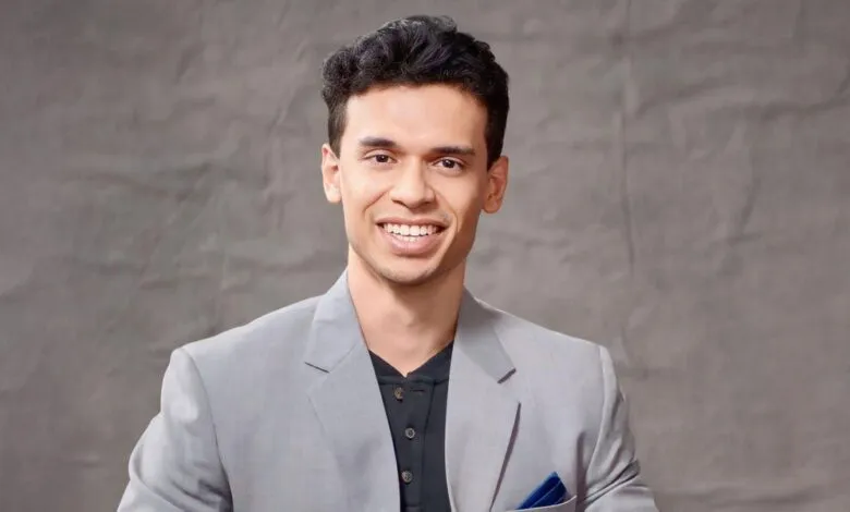 Portrait of a smiling man in a gray suit against a gray backdrop.