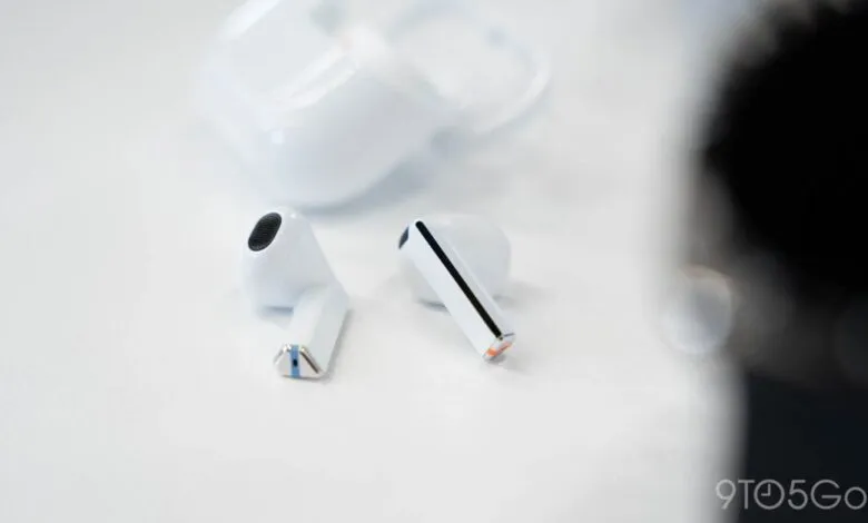 Close-up of white wireless earbuds and charging case on a white surface.