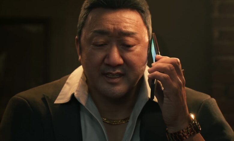 Ma Dong-seok on phone, wearing suit and gold chain.