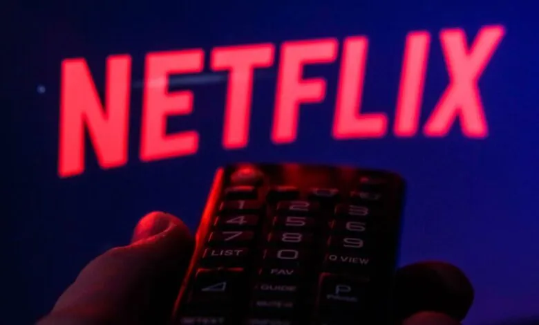 Hand holds remote in front of Netflix logo on a screen.