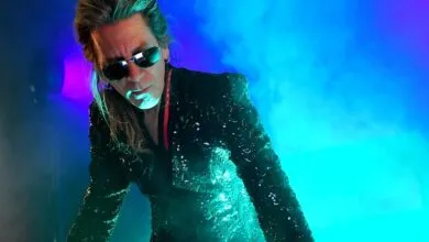 Musician with sunglasses and sequined jacket on stage.