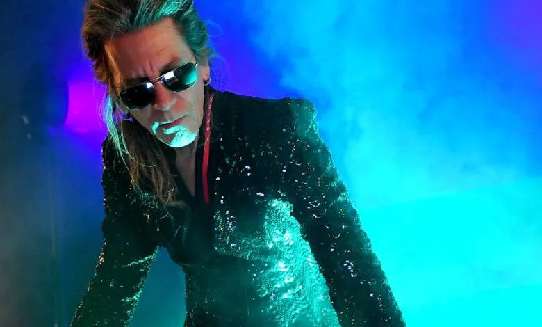 Musician with sunglasses and sequined jacket on stage.