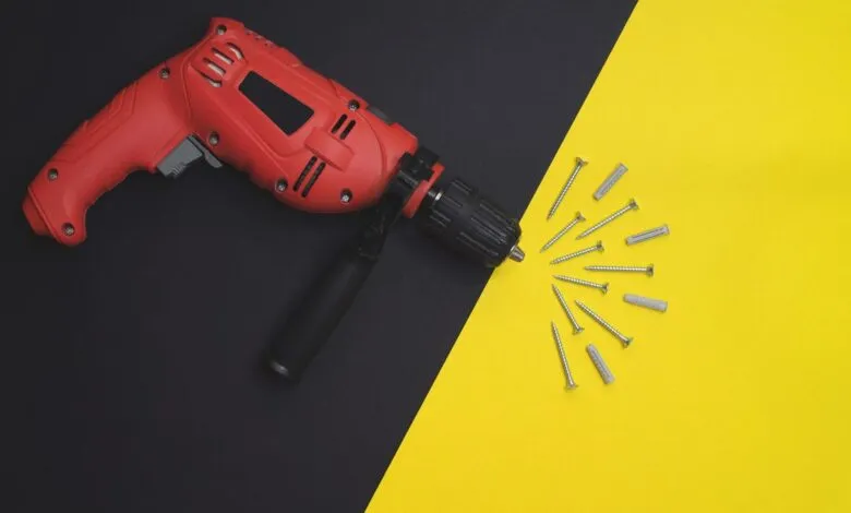 Red power drill and screws arranged on a black and yellow background.