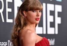 Taylor Swift poses in red dress with long wavy hair and red lipstick.