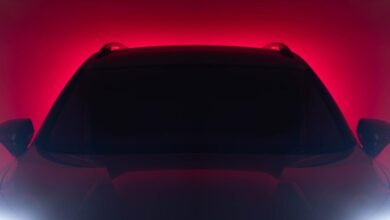 Close-up of a car's front end with a dark silhouette against a red background.